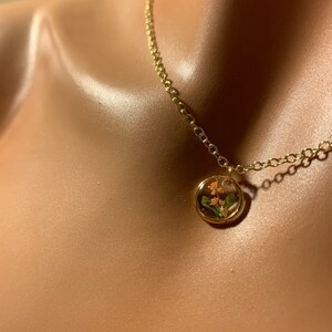 以下が含まれることがあります： ピンクとグリーンの押し花が施された丸いペンダントが付いたゴールドチェーンネックレスです。