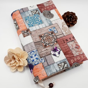 Könnte beinhalten: Ein Buchumschlag mit Patchwork-Design in verschiedenen Brauntönen, Orange, Blau und Weiß. Das Design beinhaltet ein Herz, Paisley-Muster und die Wörter "Jardin" und "Provence".
