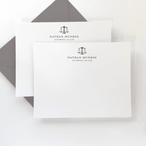 May include: Two white stationery cards with a gray envelope. The cards feature a black and white scale of justice logo and the text "Nathan Munroe Attorney at Law".