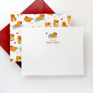 May include: A white card with a capybara illustration and the text "A note from Tinley Reese". The card is on top of a red envelope with a pattern of capybaras.