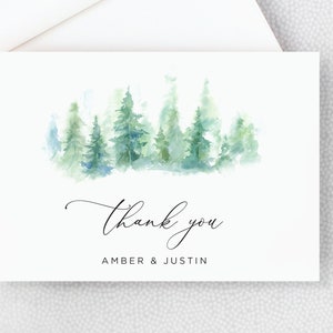 May include: A watercolor thank you card with a green and blue watercolor illustration of a forest. The text "Thank you" is written in cursive script below the illustration, followed by "Amber & Justin".