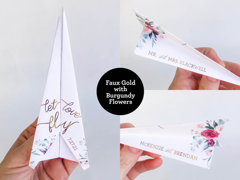 May include: White paper airplane with gold lettering that reads "let love fly" and the date 7.27.21. The airplane has floral accents with burgundy flowers. The text "Faux Gold with Burgundy Flowers" is in a black circle. Other airplanes have names.