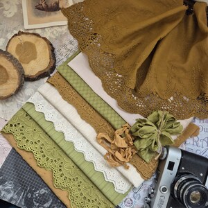 Op de afbeelding: Een assortiment stoffen stalen in groen, wit en bruin, met verschillende kant- en patroonontwerpen. Een vintage camera en decoratieve houten schijfjes dragen bij aan de rustieke sfeer.