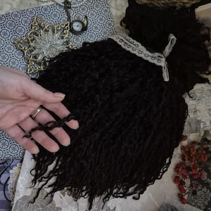 May include: A black curly wool roving with a white lace ribbon tied around it.