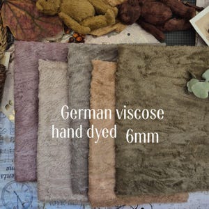Può includere: Cinque campioni di tessuto in viscosa tedesca tinti a mano nelle tonalità malva, beige, grigio, marrone chiaro e verde oliva. Il tessuto ha un pelo di 6 mm e una consistenza morbida e pelosa. Il testo "German viscose hand dyed 6mm" è visibile.