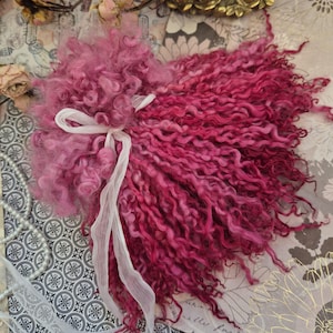 May include: Pink and white curly yarn with a white ribbon tied around it. The yarn is on a patterned background.