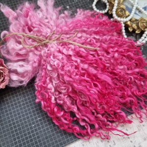 May include: A bundle of pink and white curly yarn with a gradient from white to pink. The yarn is tied together with a brown twine.