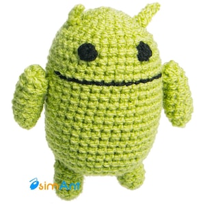 Może przedstawiać: Zielona pluszowa zabawka w kształcie maskotki Androida, wykonana na szydełku. Zabawka ma czarne oczy i czarne usta.