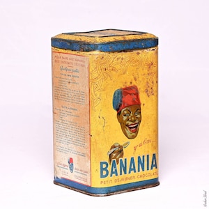 Peut inclure: Une boîte en métal vintage jaune et bleue avec un dessin animé souriant d'un homme portant un fez rouge. La boîte est étiquetée "Banania Petit Dejeuner Chocolate" et présente un motif de banane. La boîte contient des instructions pour faire de la crème de banane et de la soupe de banane.