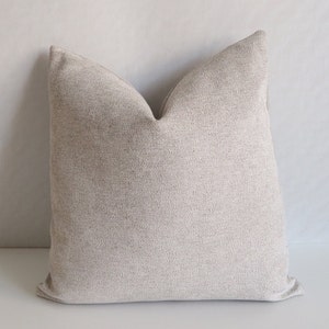 May include: A beige throw pillow with a textured fabric. The pillow is square shaped and has a simple design.