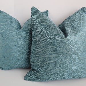 May include: Two teal blue throw pillows with a woven, textured pattern. The pillows are made of a soft, plush fabric.