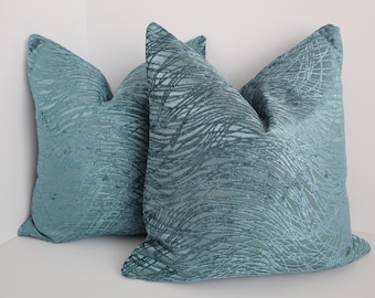 Puede incluir: Dos almohadas de tiro azul turquesa con un patrón tejido texturizado. Las almohadas están hechas de una tela suave y mullida.