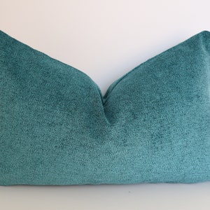 May include: A teal blue throw pillow with a textured fabric. The pillow is rectangular and has a simple design.