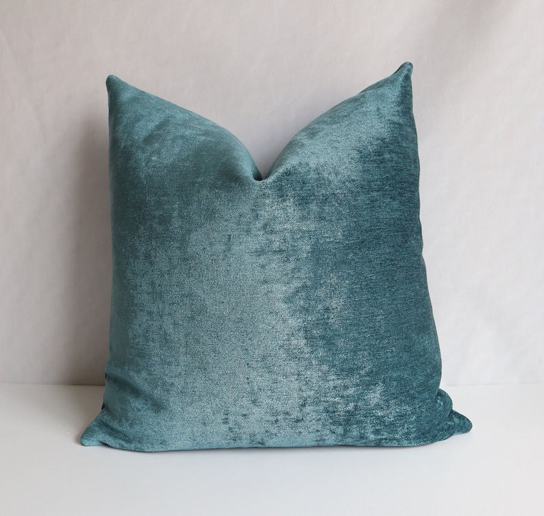 Puede incluir: Almohada de terciopelo azul turquesa con una superficie suave y texturizada. La almohada es de forma cuadrada y tiene un dise&ntilde;o sencillo.