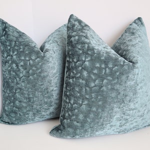 May include: Two teal blue decorative throw pillows with a textured, patterned fabric.