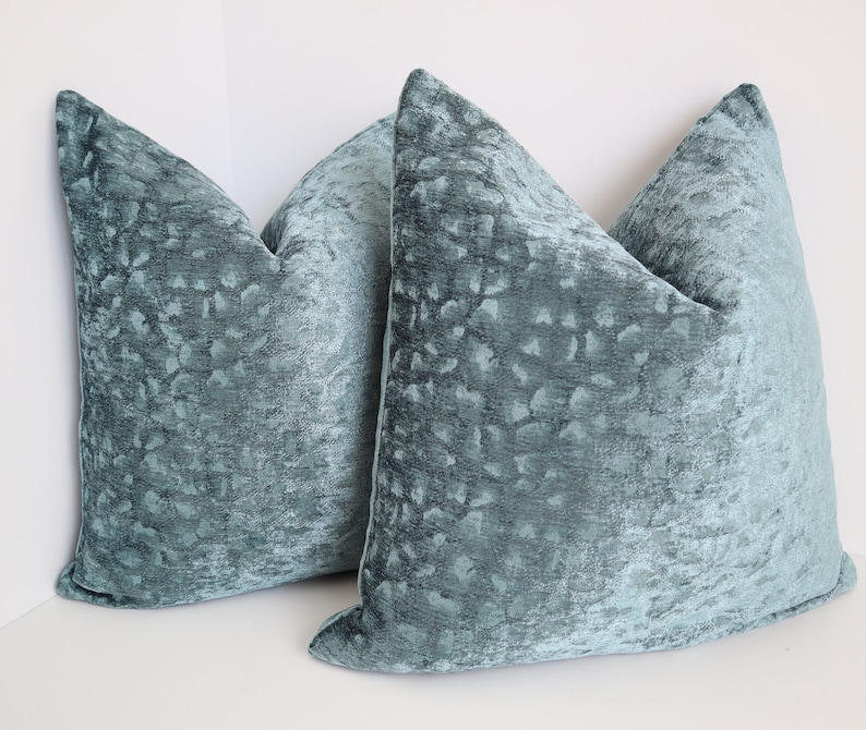May include: Two teal blue decorative throw pillows with a textured, patterned fabric.