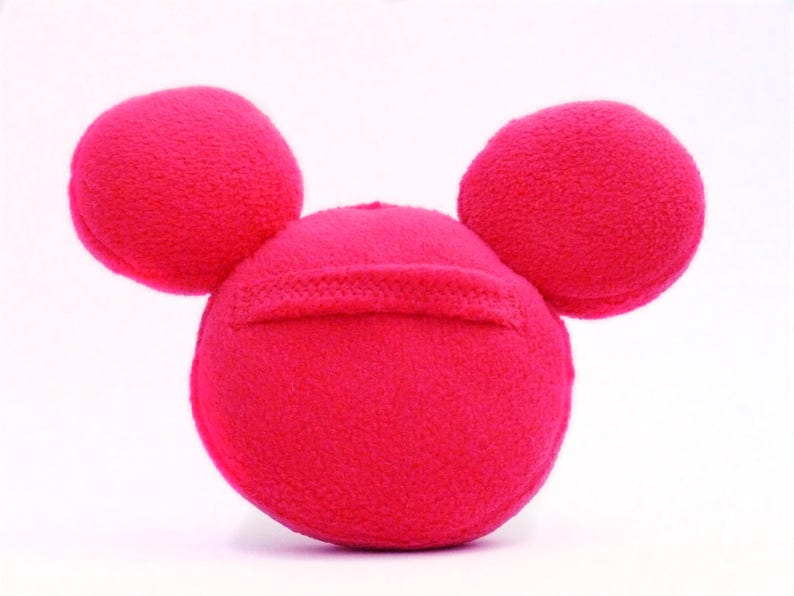 May include: A vibrant pink plush toy in the shape of a mouse's head, with a round head and two circular ears. The toy has a soft, textured surface and is set against a white background.
