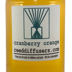 May include: A yellow bottle with a white lid and a white label. The label has a green logo and the text "cranberry orange reeddiffusers.com". The text "Keep out of reach of children and pets - Not for consumption." is also on the label.