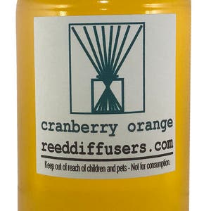 May include: A yellow glass bottle with a white lid and a white label. The label has a green logo and the text "cranberry orange reeddiffusers.com". The text "Keep out of reach of children and pets - Not for consumption." is also on the label.