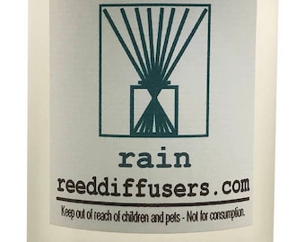 May include: A clear glass bottle with a white cap and a label that says "rain reeddiffusers.com". The label also has a graphic of a reed diffuser with a geometric design. The text "Keep out of reach of children and pets - Not for consumption." is on the label.