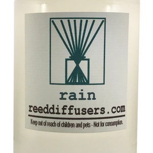 May include: A clear glass bottle with a white cap and a label that says "rain reeddiffusers.com". The label also includes a graphic of a reed diffuser and the text "Keep out of reach of children and pets - Not for consumption."