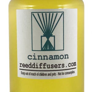 May include: A clear glass bottle with a white cap filled with yellow liquid. The label reads "cinnamon reeddiffusers.com" and "Keep out of reach of children and pets - Not for consumption."