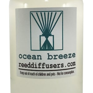 May include: A clear glass bottle with a white cap and a white label. The label has a green logo of reeds in a vase and the text "ocean breeze reeddiffusers.com". The label also includes the text "Keep out of reach of children and pets - Not for consumption."