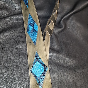 May include: A brown leather guitar strap with blue and black diamond-shaped patterned leather accents.