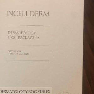 Op de afbeelding: Een witte kaart met de tekst "INCELLDERM" in grote, vetgedrukte letters bovenaan. Onder de tekst bevindt zich een kleinere tekstbox met de woorden "DERMATOLOGY FIRST PACKAGE EX". Daaronder bevindt zich een andere tekstbox met de woorden "PRESTIGE CARE SHINE THE MOMENTS". Onderaan de kaart staat de tekst "DERMATOLOGY BOOSTER EX".