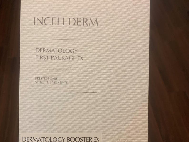 Op de afbeelding: Een witte doos met de tekst "INCELLDERM" in zwart bovenaan. De tekst "DERMATOLOGY FIRST PACKAGE EX" staat in zwart onder de bedrijfsnaam. De tekst "PRESTIGE CARE SHINE THE MOMENTS" staat in zwart onder de pakketnaam. De tekst "DERMATOLOGY BOOSTER EX" staat in zwart onderaan de doos.
