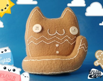 May include: A brown gingerbread cat plush toy with white stitching and buttons for eyes. The cat is sitting on a blue background with clouds and a sun.