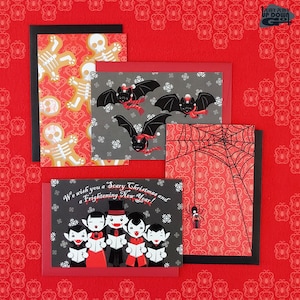 May include: Set of four Halloween-themed greeting cards. The cards feature a black and white skeleton pattern, a black bat on a gray background with snowflakes, a black spider web on a red background, and a group of vampires singing Christmas carols on a black background. The text on the card reads "We wish you a Scary Christmas and a Frightening New Year!"