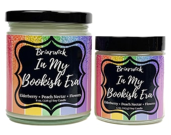 Puede incluir: Dos velas en frasco de vidrio con tapas negras. Las etiquetas dicen "Briarwick In My Bookish Era" con acentos de arcoíris. La vela más grande es de 226 g y la más pequeña de 113 g. La fragancia es Saúco + Néctar de melocotón + Flores.