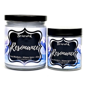 May include: Two glass candle jars with black lids and labels. The labels are white with black text and feature a mountain scene. The larger jar is 8 ounces and the smaller jar is 4 ounces. Both jars are labeled "Briarwick Resonance Cozy Blankets + Winter Spice + Khui Soy Candle".