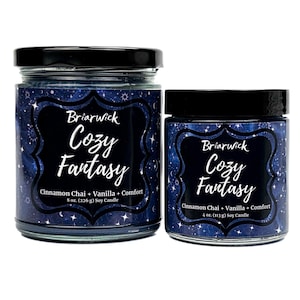 May include: Two glass jar candles with black lids. The labels feature a dark blue background with a starry design and the words "Briarwick Cozy Fantasy". The text below reads "Cinnamon Chai + Vanilla + Comfort". The larger candle is 226 g.