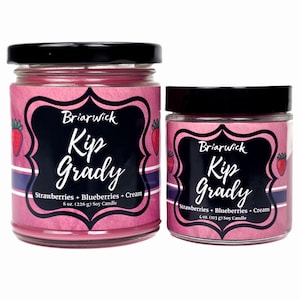 May include: Two glass jars of soy candles with black lids. The labels are pink with a black frame and the text "Briarwick Kip Grady Strawberries + Blueberries + Cream". One jar is 226 g, the other is 113 g.
