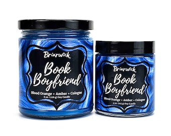 May include: Two blue glass candle jars with black lids. The larger jar is 8 ounces and the smaller jar is 4 ounces. Both jars have a white label with the text "Briarwick Book Boyfriend" and the scent description "Blood Orange + Amber + Cologne".