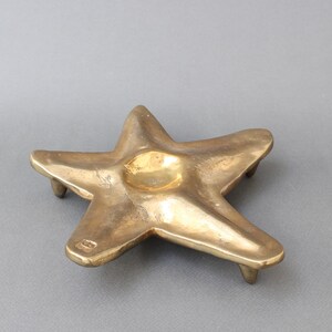 May include: A brass starfish-shaped trinket dish with a raised center and five points. The dish has a smooth, polished finish and a slightly aged patina.