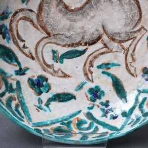 May include: A white ceramic bowl with a blue and green floral design. The bowl features a stylized animal design in brown and white.