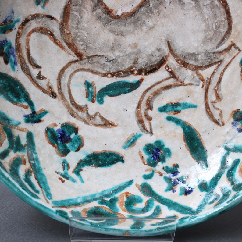 May include: A white ceramic bowl with a blue and green floral design. The bowl features a stylized animal design in brown and white.
