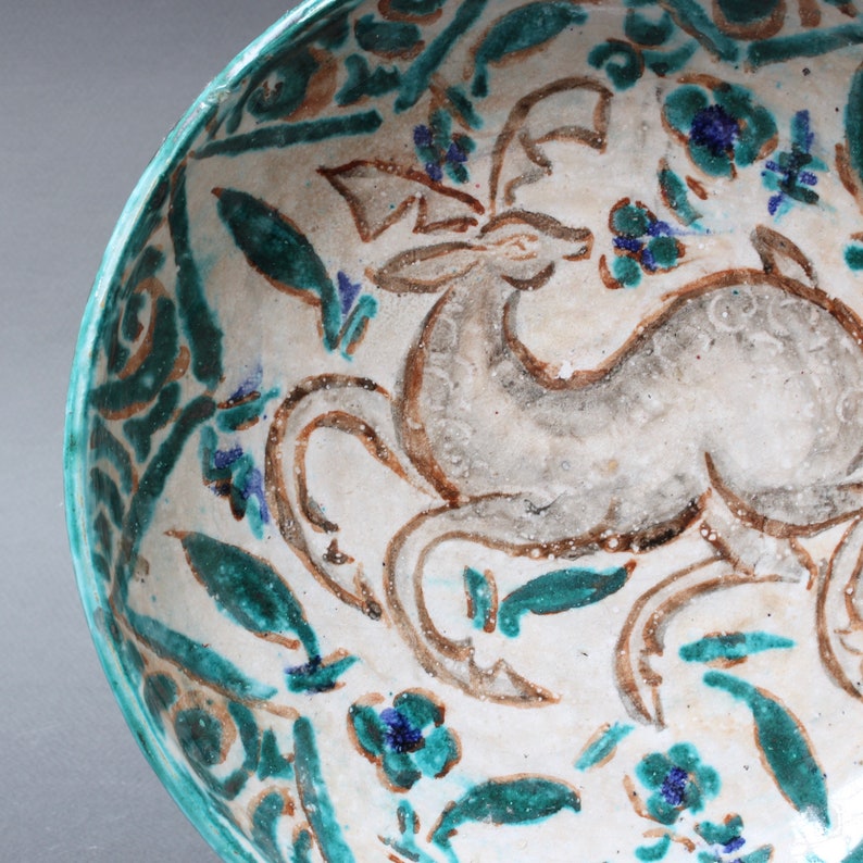 May include: A white ceramic bowl with a green and brown floral design and a stylized deer in the center.