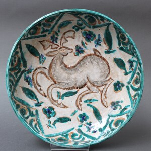 May include: A white ceramic bowl with a green and brown glaze. The bowl features a stylized deer design in the center, surrounded by floral motifs.