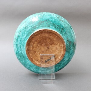 May include: A large, round ceramic plate with a turquoise glaze. The plate has a brown, unglazed base.