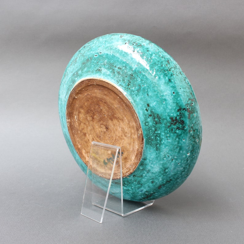 May include: A teal ceramic plate with a brown interior. The plate is on a clear acrylic stand.