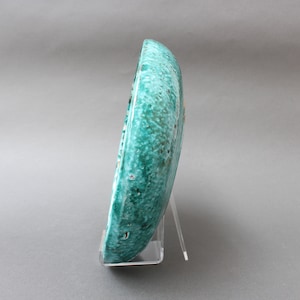 May include: A teal ceramic plate with a textured surface. The plate is on a clear acrylic stand.