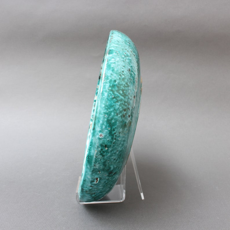May include: A teal ceramic plate with a textured surface. The plate is on a clear acrylic stand.