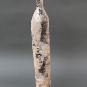 May include: A tall, slender ceramic vase with a white and black glaze. The vase has a textured surface and a rounded bottom.