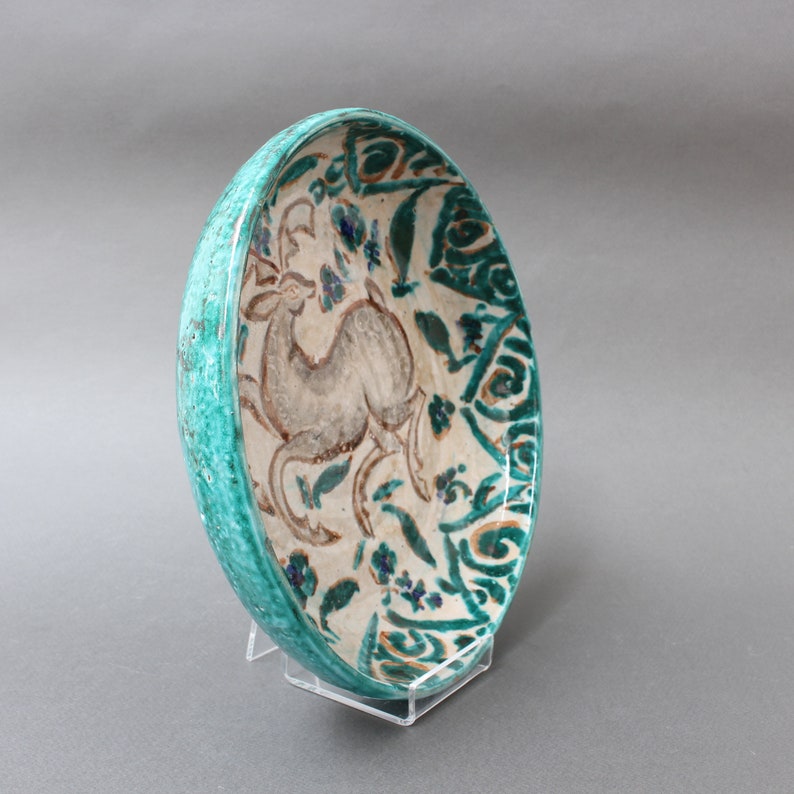 May include: A turquoise ceramic bowl with a white glaze and a painted design of a deer in a floral pattern.