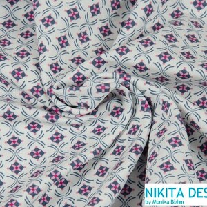 Könnte beinhalten: Weißer Stoff mit einem sich wiederholenden Muster aus rosa und blauen geometrischen Formen. Der Stoff ist gefaltet und trägt ein Etikett mit der Aufschrift "NIKITA DESIGN by Monika Böhm".