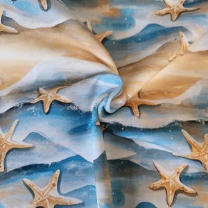 Könnte beinhalten: Stoff mit einem Aquarelldesign mit Seesternen, die über eine Strandszene verstreut sind. Der Stoff hat eine Farbpalette aus Blau, Beige und Weiß, wobei die Seesterne einen hellbraunen Farbton haben. Das Design erinnert an ein Küstenmotiv.